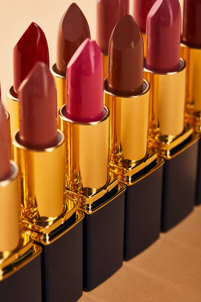 close up of various red shades of lipstick in tubes on beige 