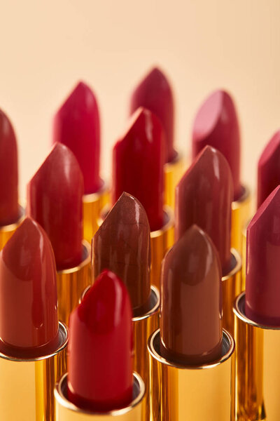 selective focus of various red shades of lipstick in tubes isolated on beige 