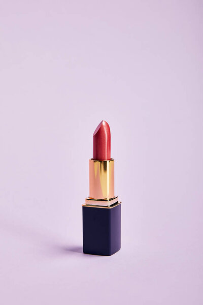 single opened tube of red lipstick on purple