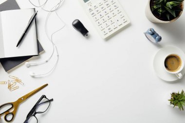 beyaz yüzeyüzerinde bitkiler, camlar, kahve, kulaklık ve ofis malzemeleri üst görünümü