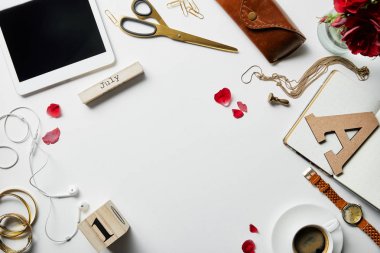 beyaz yüzeyde dijital tablet, kulaklık, takı, kasa, çiçek, ofis malzemeleri ve kahve üst görünümü