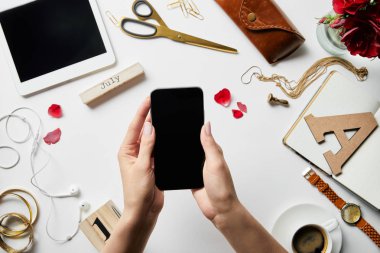 dijital tablet, kulaklık, takı, kasa, çiçek, ofis malzemeleri ve beyaz yüzeyüzerinde kahve üzerinde elinde akıllı telefon tutan kadın kırpılmış görünümü