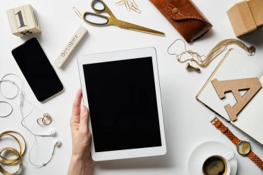 akıllı telefon, kulaklık, takı, kasa, çiçek, ofis malzemeleri ve beyaz yüzeyüzerinde kahve yakınında dijital tablet tutan kadın kırpılmış görünümü
