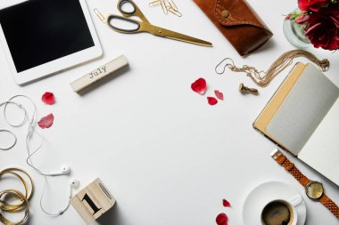 beyaz yüzeyde dijital tablet, takı, kulaklık, kasa, çiçek, ofis malzemeleri ve kahve üst görünümü