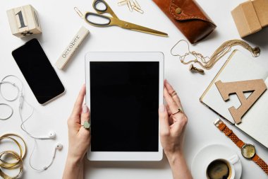 akıllı telefon, kulaklık, takı, kasa, çiçek, ofis malzemeleri ve beyaz yüzeyüzerinde kahve yakınında elinde dijital tablet tutan kadın kırpılmış görünümü
