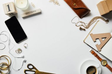 akıllı telefon, not defteri, mum, kasa, kulaklık, bitki, ofis malzemeleri ve beyaz yüzey üzerinde takı ile kahve üst görünümü