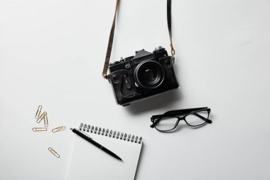 beyaz yüzeyde kalem ve kırtasiye ile fotoğraf makinesi, gözlük, not defteri üst görünümü