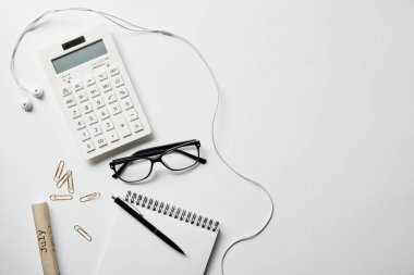 kırtasiye, hesap makinesi, kulaklık ve beyaz yüzeyli kalem ile dizüstü üst görünüm