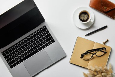 beyaz yüzeyüzerinde gözlük, kahve, kasa ve not defteri yakınında dizüstü üst görünümü