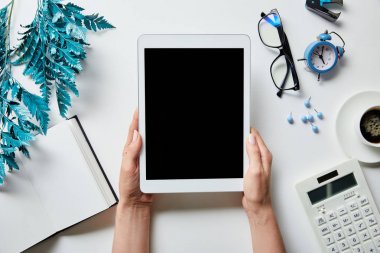 not defteri, kahve, kırtasiye, çalar saat, hesap makinesi, gözlük ve beyaz yüzey üzerinde mavi şube yakınında elinde dijital tablet tutan kadın kırpılmış görünümü