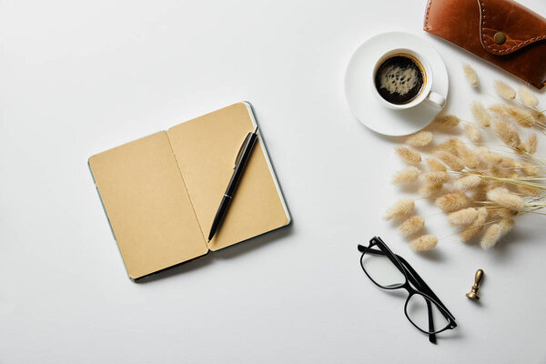 top view of notepad with pen, coffee, glasses and case on white surface