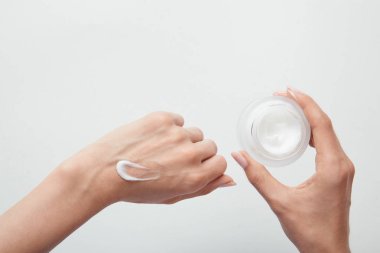 cilde krem uygulayan ve beyaz üzerine izole kavanoz tutan kadının kırpılmış görünümü