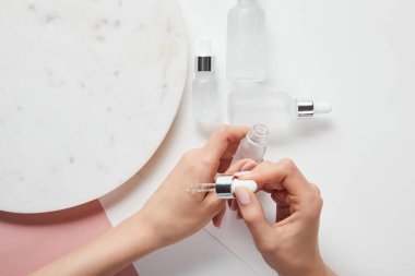 beyaz pembe yüzeyüzerinde kozmetik cam şişe ve plaka yakın el üzerinde sıvı uygulayan kadın kırpılmış görünümü