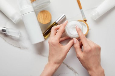 tüpler, kozmetik dispenser ve beyaz yüzeyüzerinde göz fırçası ile cam şişe yakın krem ile kavanoz tutan kadın kırpılmış görünümü