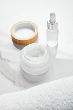 opened jar with cosmetic cream and glass bottle near towel on white surface clipart