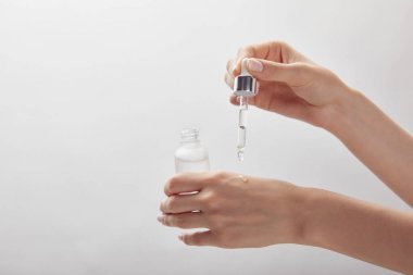 kozmetik cam şişe tutan kadın kırpılmış görünümü, cilde nemlendirici serum uygulayarak