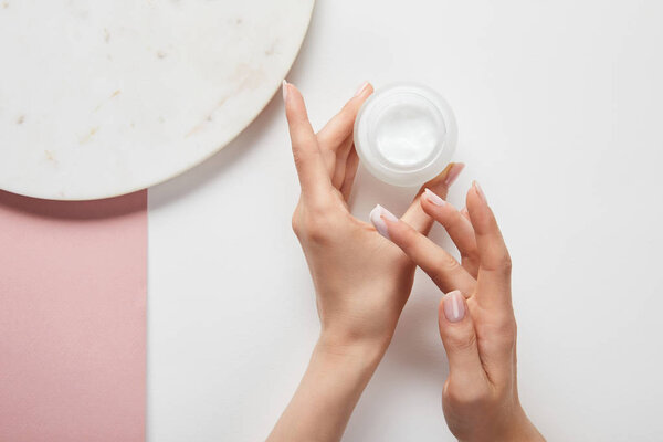 cropped view of woman holding cream in jar, applying cosmetic on skin