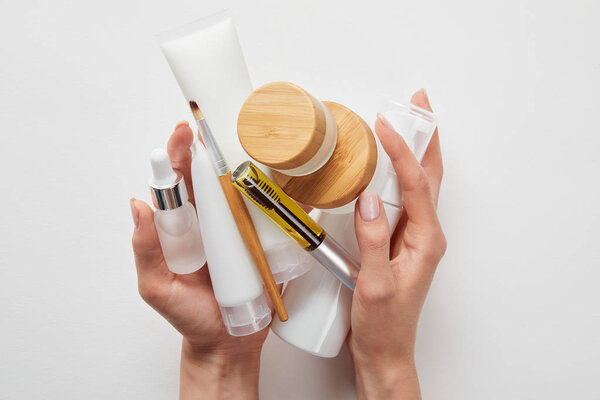 обрезанный вид женских рук с косметикой в трубах, автоматах, бутылках и банках, изолированных на белом
