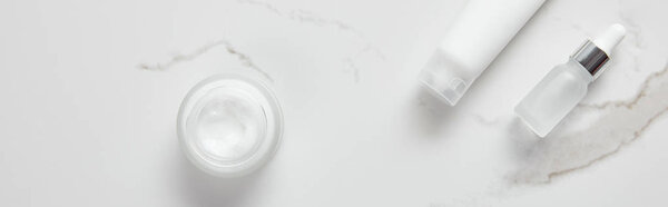 panoramic shot of cosmetic glass bottle, jar with cream and moisturizer tube on white surface