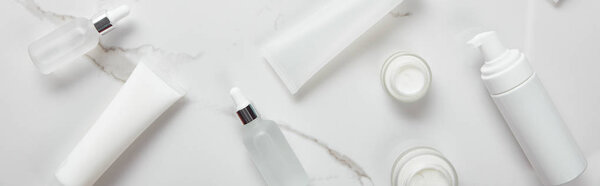 panoramic shot of cosmetic glass bottles, jars with cream, moisturizer tubes and dispenser on white surface