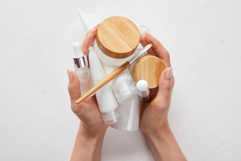 cropped view of woman hands with cosmetics in tubes, dispensers, bottles and jar isolated on white