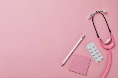pembe arka plan üzerinde stetoskop, kalem, kağıt parçası ve blister paketi üst görünümü
