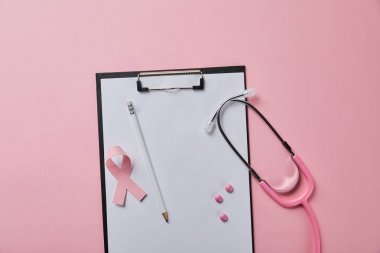 pembe arka plan üzerinde stetoskop yakın boş kağıt ile klasörüzerinde kalem, pembe hap ve meme kanseri kurdele