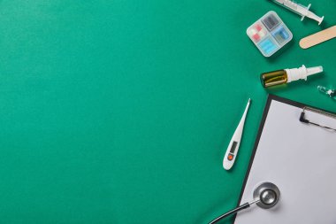 şırınga, ahşap dil depresörü, ampul, hap kutusu, burun spreyi, termometre, stetoskop ve yeşil arka plan üzerinde klasör