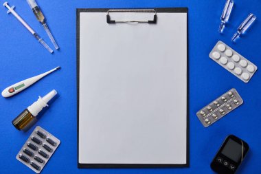 mavi yüzeyüzerinde çeşitli tıbbi malzemeler tarafından yuvarlak boş kağıt ile klasörün üst görünümü