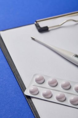 blister paketi ve termometre seçici odak klasörüzerinde boş kağıt mavi izole