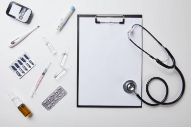 beyaz üzerinde boş kağıt ve stetoskop ile klasöryakınında çeşitli tıbbi malzemelerin üst görünümü 