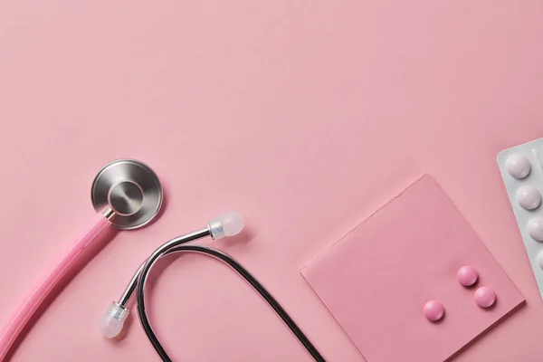 ピンクの聴診器のトップビュー 薄いピンクの背景に紙とブリスターパックの3つの錠剤 — ストック写真