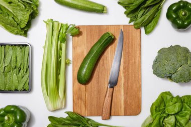 top view of green vegetables and wooden chopping board with knife on white background clipart
