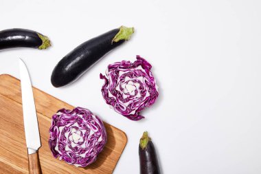top view of red cabbage and eggplants on wooden chopping board and knife on white background clipart