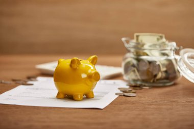 selective focus of bankruptcy form, coins, yellow piggy bank and glass jar with dollar banknotes on wooden table clipart