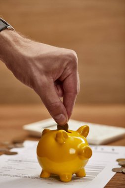 partial view of man putting coin in yellow piggy bank clipart