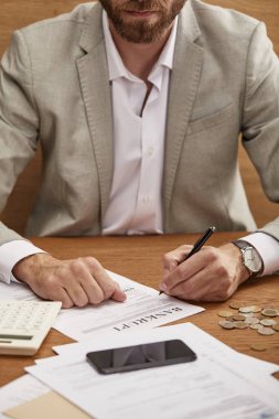 cropped view of bearded businessman in suit filling in bankruptcy form at wooden table clipart