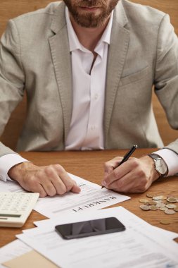 cropped view of bearded businessman in suit filling in bankruptcy form at wooden table clipart