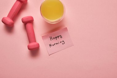 turuncu suyu üst görünümü, pembe dambıl ve pembe arka plan üzerinde mutlu sabah yazı ile yapışkan not