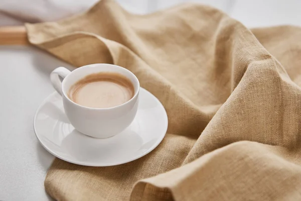 Bej Peçete Yakınında Tabak Üzerinde Beyaz Fincan Kahve Yakın Görünümü — Stok fotoğraf