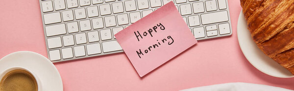 top view of computer keyboard and pink sticky note with happy morning lettering near croissant and coffee on pink background, panoramic shot