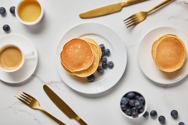 top view of pancakes, cup of coffee and scattered blueberries near golden cutlery clipart