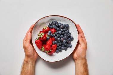 cropped view of man holding big plate with tasty strawberries and blue berries clipart