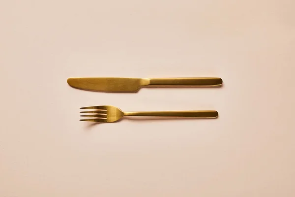 ピンクの背景に金色のフォークとナイフのトップビュー — ストック写真