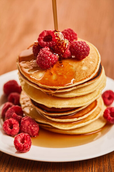 close up view of plate with pancakes and raspberries with syrup 