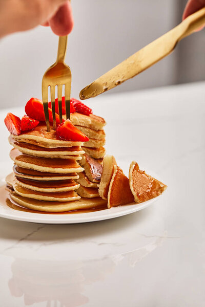 cropped view of man cutting pancakes with strawberries