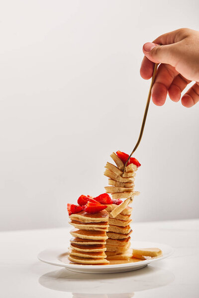 cropped view of man taking slice of pancakes with golden fork from white plate 