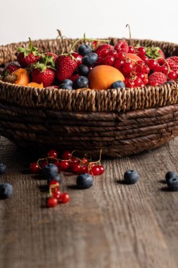 close up view of ripe seasonal berries and apricots in wicker basket on wooden table isolated on white clipart