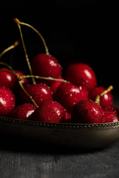 wet delicious cherries in metal basket on wooden dark table isolated on black