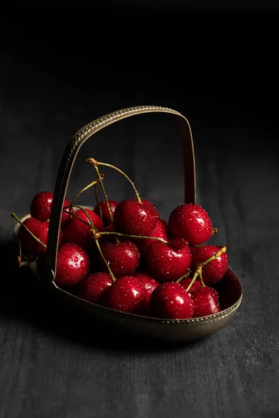 红色美味的湿樱桃在金属篮子在木制深色桌子上隔离在黑色 — 图库照片
